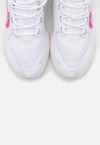 White athletic shoes with pink and gray accents, featuring a mesh upper, padded tongue, and rubber sole, viewed from above.
