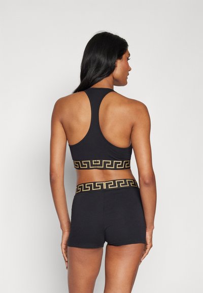 Svart sportig crop-top med racerback-design och ett geometriskt mönster i guld på midjebandet, parat med svarta sportshorts.