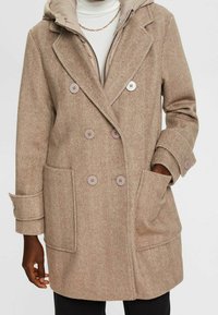 Dwurzędowy płaszcz w jodełkę w kolorze brązowym z odpinanym pikowanym kapturem, dużymi przednimi kieszeniami i okrągłymi guzikami.