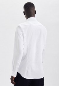 Camicia bianca a maniche lunghe con colletto classico, polsini con bottone e tessuto liscio. Caratterizzata da una vestibilità su misura e dettagli di cucitura sottili.