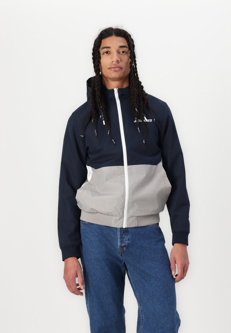 Marineblauer und grauer Reißverschlussjacke mit Kapuze, die elastische Bündchen und ein leichtes Material bietet. Mit einem Logo auf der Brust und einer lässigen Passform.