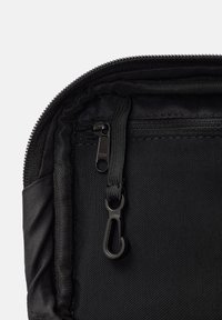 Pocchetto in tessuto nero con chiusura a zip, caratterizzato da una superficie testurizzata, molteplici scomparti interni e una robusta linguetta per apertura.