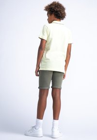 Polo skjorte i lys gul med sort piping, kombineret med olivengrønne shorts. Hvide sneakers og sportsokker fuldender outfittet.