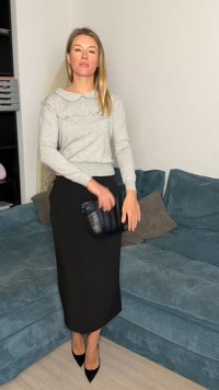 Top gris de manga larga con cuello con volantes, combinado con una falda lápiz negra y tacones negros de punta afilada, llevando un bolso de mano negro.