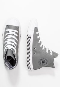 Baskets montantes en cuir gris avec embout en caoutchouc blanc et design à lacets. Présentent un motif chevron noir et blanc sur la semelle.