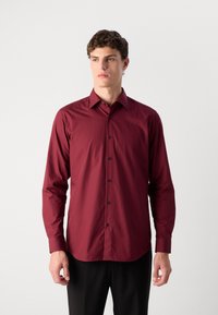 Bordeaux langærmet skjorte med klassisk krave, sorte knapper og glat tekstur; båret med sorte bukser, som fremviser en tætsiddende design.