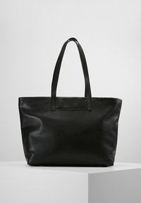 Černá kožená taška přes rameno s dvěma dlouhými držadly, hladkým povrchem a minimalistickým designem. Žádné viditelné kovové prvky ani vzory.