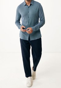 Vaaleansininen pitkähihainen paita, jossa on napit ja kaulus, yhdistetty tummansinisiin housuihin ja valkoisiin lenkkareihin, neutraalilla taustalla.