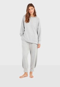 Grijze sweatshirt en bijpassende joggingsbroek van zachte stof. De sweatshirt heeft een relaxte pasvorm en een ronde halslijn; de broek heeft geknoopte enkels.