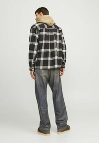 Tjekket flannel skjorte i sort, hvid og bordeaux, lagdelt over en beige hættetrøje. Løse, mørke denim jeans og brune sko fuldender looket.