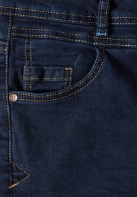 Donkerblauwe denimstof met een zichtbare textuur, voorzien van contrasterende beige stiksels en een klein zakontwerp met een metalen knoop.