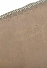 Brūnas ādas maks ar gludu faktūru, ar sudraba rāvējslēdzēju un smalkām šuvju detaļām. Taisnstūrveida forma, minimālistisks dizains.