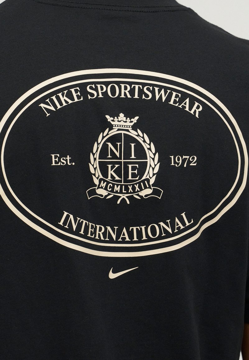 Maglietta nera sul retro con logo bianco Nike Sportswear International, stemma con "NIKE" e numeri romani "MCMLXXII" e piccolo swoosh sotto.