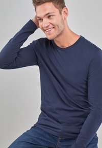 Marineblå langærmet T-shirt lavet af bomuld med rund halsudskæring. Glat tekstur, tætsiddende design, bæres med blå jeans.