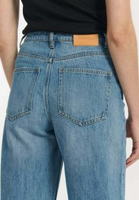 Jasnoniebieskie dżinsy z wysokim stanem, prostymi nogawkami i skórzaną naszywką z wytłoczonym logo. Zawierają dwie tylne kieszenie.