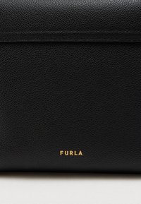 Crni kožni novčanik s teksturom i zlatnim «FURLA» logom urezanim blizu donjeg centra na bijeloj površini.