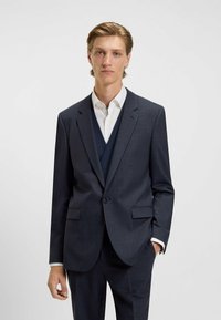 Mörkblå rutmönstrad kostym med en blazer med två knappar, matchande väst och en vit skjorta. Har smala slag och sidofickor.