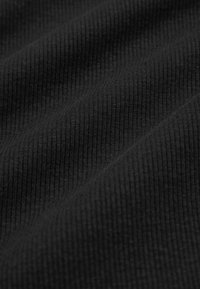 Musta ribbattu kangas, jossa on teksturoitu pinta, jossa on pystyraitoja ja pehmeä, joustava laatu, joka on ideaalinen erilaisille vaatteille.