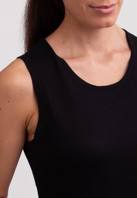 Top nero senza maniche con una trama liscia e scollatura ampia, che mostra un primo piano della scollatura e dell'area delle spalle.