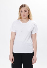 Camiseta de algodón blanca con mangas cortas, cuello redondo, adornada con remaches plateados dispersos que aportan una textura y detalle decorativos.