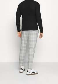 Zwarte gebreide trui, lichtgrijze geblokte broek en witte sneakers met zwarte strepen. Focus op eenvoudige, hedendaagse ontwerpelementen.