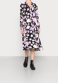 Schwarzes Kleid mit langen Ärmeln, das ein Blumenmuster in pinken und lila Farbtönen aufweist. Knielang mit einer geknöpften Vorderseite und einer lässigen Passform.