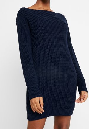 Vestido de punto en azul marino, con textura acanalada, mangas largas y escote tipo hombros descubiertos. Largo hasta la mitad del muslo, ajuste relajado.