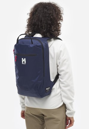 Dunkelblaues Rucksack aus glattem, strapazierfähigem Stoff, mit einer vorderen Reißverschlusstasche, Logo und verstellbaren schwarzen Trägern. Schlankes, rechteckiges Design.