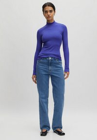 Paarse geribde coltrui gecombineerd met lichtblauwe rechtgesneden jeans. De top heeft lange mouwen en een aansluitende pasvorm.