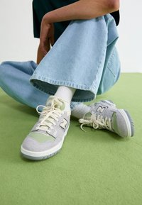 Gray and green sneakers with a suede and mesh upper. Features a textured sole, laces, and a prominent logo on the side.