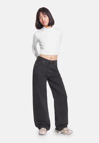 Biały, krótki top z długim rękawem i stójką, do tego czarne, szerokie spodnie jeansowe oraz jasne trampki. Gładka tekstura, casualowy styl.