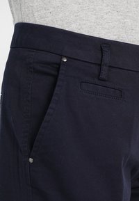 Marinblå bomullshotter med en slät textur, med en figursydd midja, sidofickor och metalldetaljer.