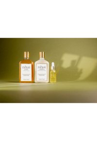 Trois produits capillaires Rahua sur une surface verte avec des ombres douces : shampooing, après-shampooing et un petit flacon compte-gouttes d’élixir.
