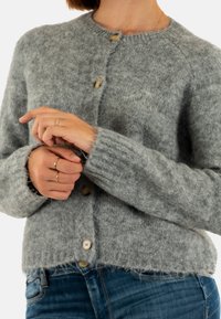 Cárdigan gris de punto con escote redondo, puños acanalados y tres botones grandes, fabricado con una tela texturizada y acogedora.