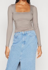 Långärmad topp med fyrkantig halsringning i ljusgråt tyg med rynkdetaljer, matchad med en ljusblå denimkjol med slits framtill.