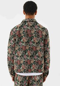 Mønstret jakke med blomster i mørkt stof, prydet med et rosemotiv i forskellige farver. Kraven er spids, med en normal pasform og lange ærmer.