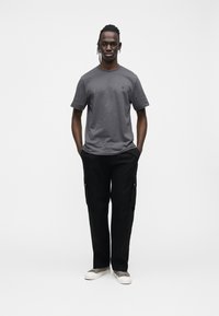 Szara bawełniana koszulka z krótkimi rękawami i logo na przodzie. Czarne spodnie typu cargo z bocznymi kieszeniami. Białe trampki z szarymi akcentami.