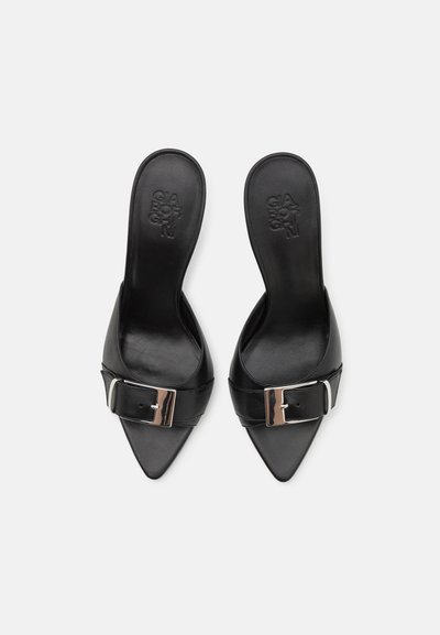 Black leather mules with a pointed toe, featuring a wide strap and a metallic buckle detail. Smooth texture and minimalist design.