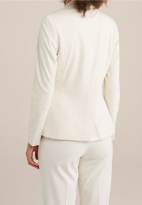 Biała dopasowana marynarka o gładkiej teksturze, usztywnionym fasonie i subtelnych detalach szwów, zestawiona z pasującymi spodniami.