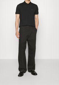 Svart polo skjorta med krage och tre-knappslåsning, kombinerad med löst sittande svarta byxor och svarta läderskor.