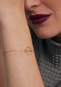 Złota bransoletka z okrągłym charmem z napisem "Mama" w delikatnym kroju pisma, przymocowanym do skręconego łańcuszka.