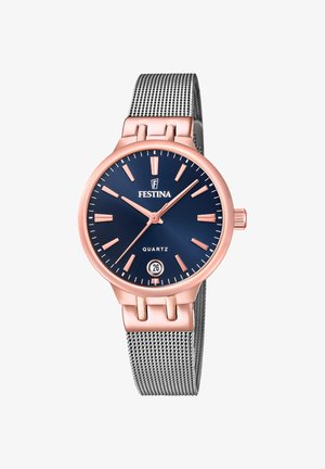 Kvarca pulkstenis ar tumši zilu ciparnīcu, rozā zelta akcentiem, datuma displeju un sudraba sieta siksniņu. Satur plānas stundu marķierus un apaļu korpusu.