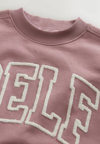 Lilla roosakas pusa soonikkoes ümmarguse kraega, esiküljel suured, tekstuuriga valged tähed. Pehme kangas siledapinna viimistlusega.