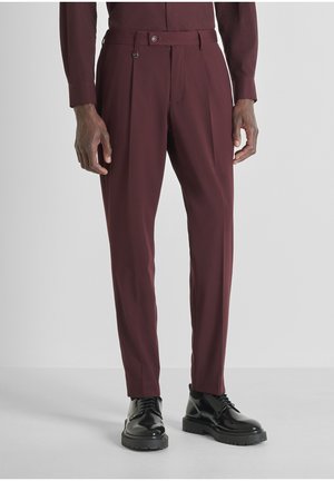Pantalones de vestir burdeos con un corte entallado, pliegues y detalles de presilla para el cinturón. Combinados con zapatos derby negros brillantes.