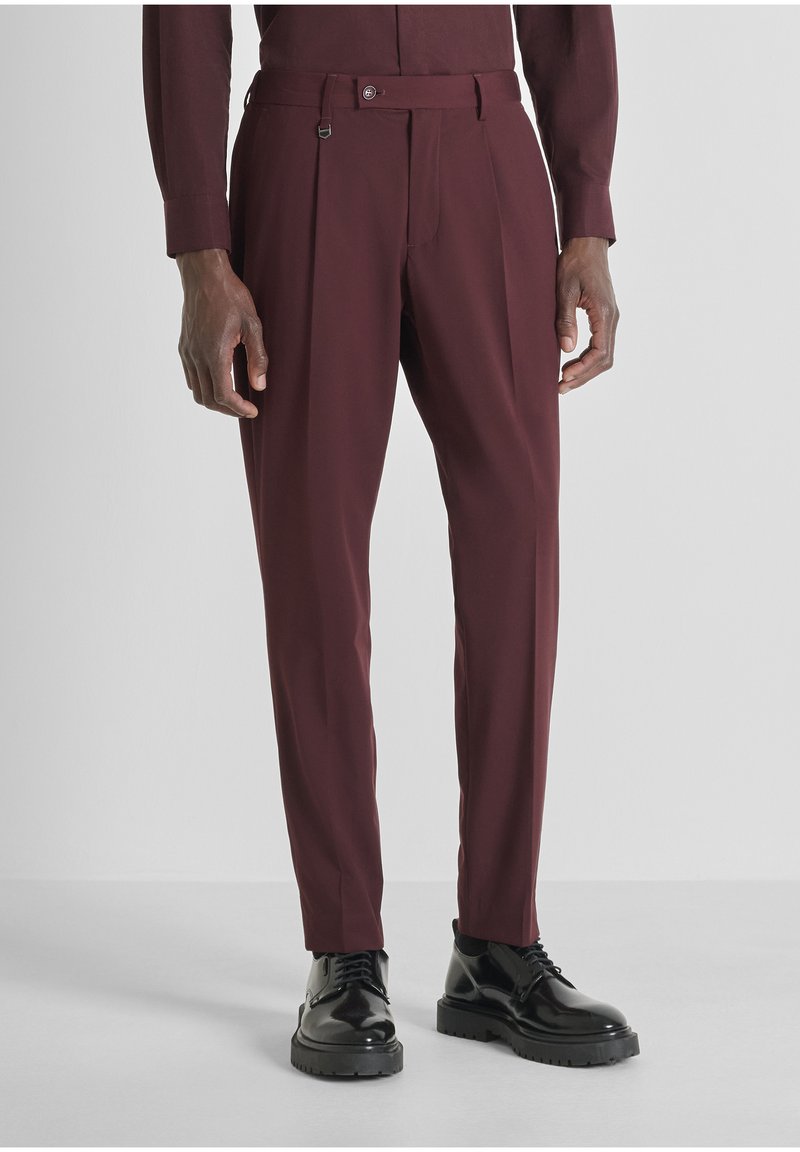 Bordeaux kleurige pantalon met een getailleerde pasvorm, plooien en een riemlus detail. Gepaard met glanzende zwarte veterschoenen.