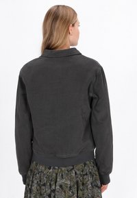 Sötét szürke farmerdzseki gallérral, bordás mandzsettákkal és szegéllyel. Az anyag texturált felülete kiegészíti a mintás zöld virágmintás szoknyát.