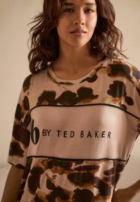 Beige kortærmet top med et brunt og sort abstrakt mønster. "B by Ted Baker" logo i sort på brystet med kontrastfarvede kanter.