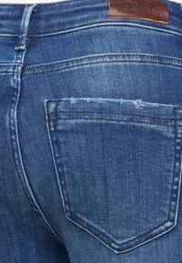 Pantalones vaqueros de mezclilla en un lavado azul medio con un clásico diseño de cinco bolsillos. Presentan costuras cosidas y un parche de cuero de la marca en la parte posterior de la cintura.