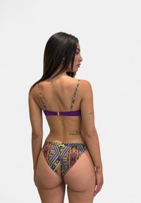 Bikini multicolore con spalline viola. Presenta vivaci motivi geometrici sui pantaloni e un dettaglio con chiusura sul retro. Texture liscia.