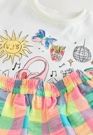 Bijela majica s grafičkim printom sunca, leptira, slušalica i pomfrita, u kombinaciji s kratkim hlačama na gumicu u više boja s kariranim uzorkom.